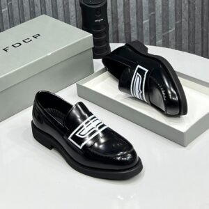 A pair of black leather loafers with white embellishment on a white table, accompanied by a gray shoe box and a black cylindrical object.