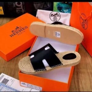 A pair of black leather Hermes Paris sandals with jute sole, nestled in an orange Hermes box, exuding luxury and sophistication.
