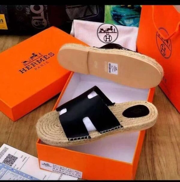 A pair of black leather Hermes Paris sandals with jute sole, nestled in an orange Hermes box, exuding luxury and sophistication.