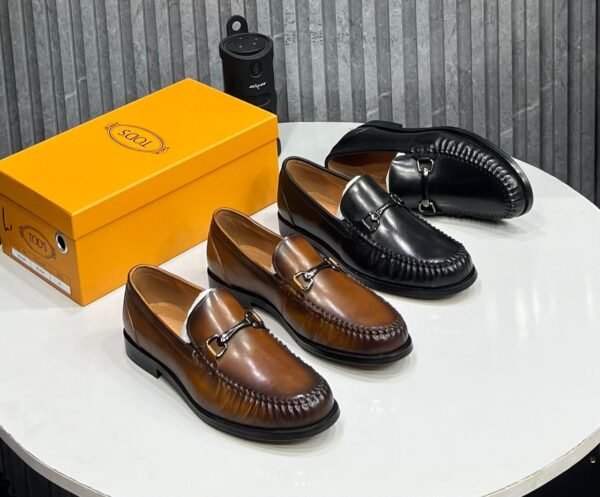 A stylish display of Tods loafers in rich brown and black leather, accompanied by the iconic yellow shoe box, showcasing the brand's commitment to quality and style.