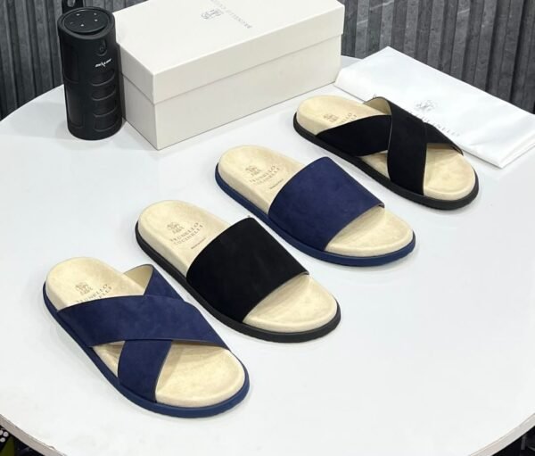 A stylish display of luxury suede slides in navy and black, accompanied by a white shoe box and dust bag, showcasing the perfect blend of comfort and elegance.