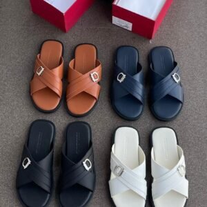 A selection of luxury double strap buckle sandals in various colors, including tan, black, navy blue, and white, displayed on a gray surface with red shoe boxes.