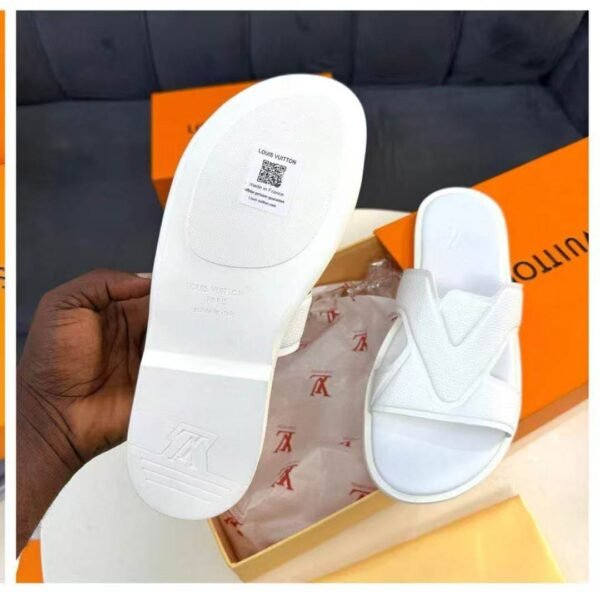 IMG-20260708-WA0052 A pair of white Louis Vuitton slides with box, dust bag, and QR code on the sole, showcasing luxury and authenticity.