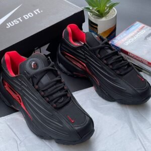 A pair of black and red Nike sneakers with a matching box and gaming console accessories on a stylish background.