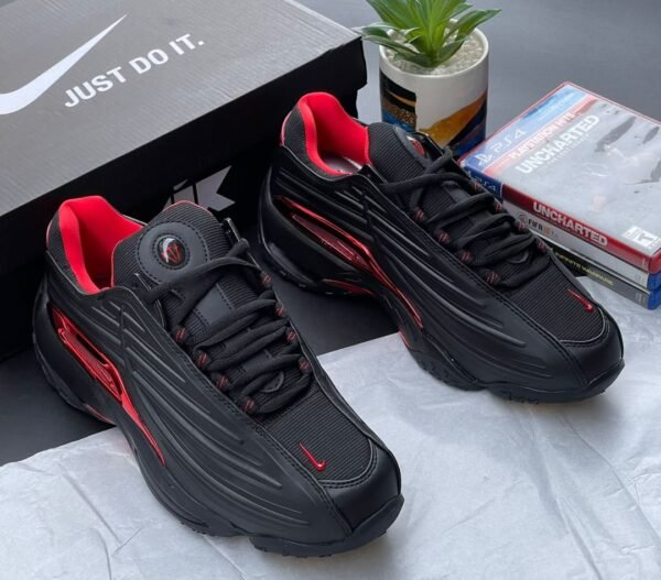 IMG-20260708-WA0056 A pair of black and red Nike sneakers with a matching box and gaming console accessories on a stylish background.