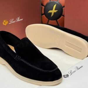 A pair of black suede loafers with cream-colored soles, displayed on a white surface with Loro Piana branding in the background.
