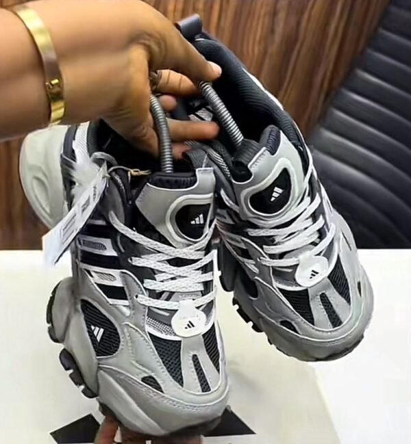 A pair of grey, black, and white Adidas Yung-96 sneakers being held by a hand, showcasing the shoe's sleek design and vibrant color scheme.