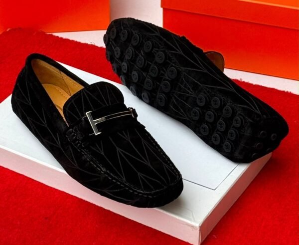 A pair of luxurious navy blue loafers with a sleek design and distinctive black buttons on the soles, presented on a white shoe box against a vibrant red background.