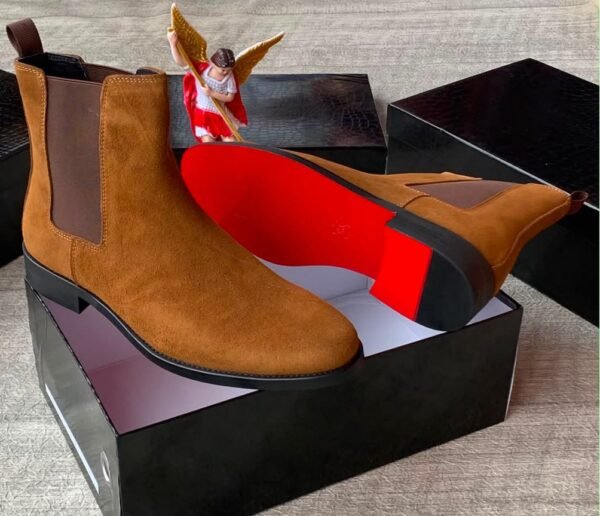 A pair of luxurious brown suede Chelsea boots with elastic sides, presented in an open black box with a red interior, exuding high-end quality and style.