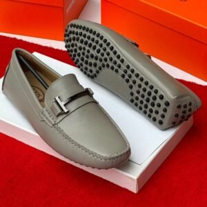 Luxury gray leather loafers with black studs on the sole, displayed on a white shoe box with an orange background.
