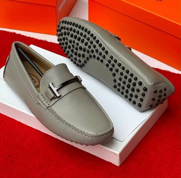 Luxury gray leather loafers with black studs on the sole, displayed on a white shoe box with an orange background.