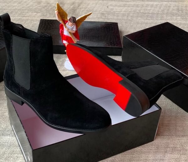 A pair of luxurious brown suede Chelsea boots with elastic sides, presented in an open black box with a red interior, exuding high-end quality and style.