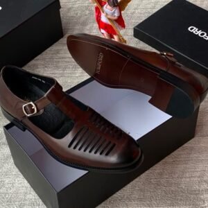 root A pair of sleek black leather monk strap shoes with a silver buckle, displayed on top of an open black shoe box alongside a small angel figurine and additional closed boxes.