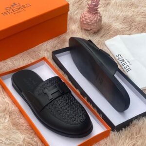 Luxury black leather Hermes slippers in an orange box on a fluffy surface