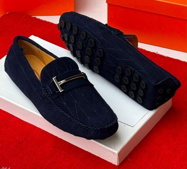 A pair of luxurious navy blue loafers with a sleek design and distinctive black buttons on the soles, presented on a white shoe box against a vibrant red background.