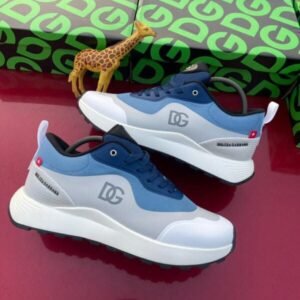 Luxury blue and white sneakers with DG logo, displayed on a red surface with green and gray boxes and a giraffe toy, Dolce & Gabbana branding