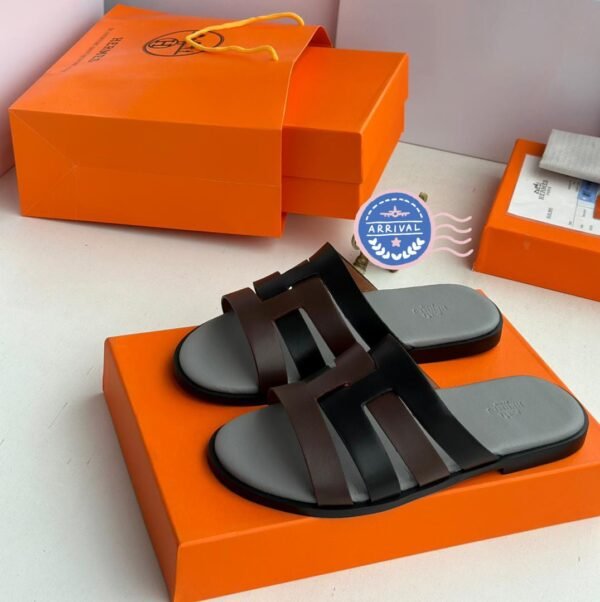 Luxury black leather sandals with two wide straps and embossed insoles, presented on an orange box with matching packaging.