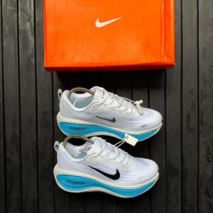 A pair of white Nike sneakers with blue soles and black Nike swoosh logo, next to an orange Nike shoe box on a dark wooden background.
