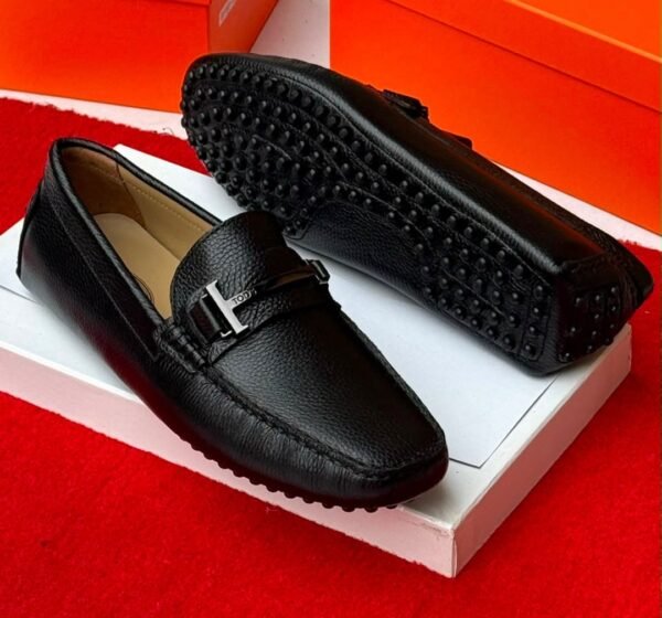 Luxury gray leather loafers with black studs on the sole, displayed on a white shoe box with an orange background.