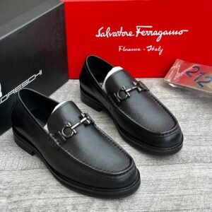 A pair of luxurious black leather loafers with metal buckles, displayed on a wooden surface with Salvatore Ferragamo box in the background.