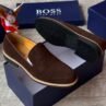 Luxury black suede loafers with tan soles and blue shoe boxes, exuding high-end style and sophistication.