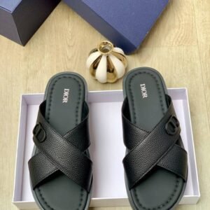 A pair of blue Dior sandals with crisscross straps and gold buckle details, nestled in a white box alongside a navy blue Dior box and a gold decorative item.