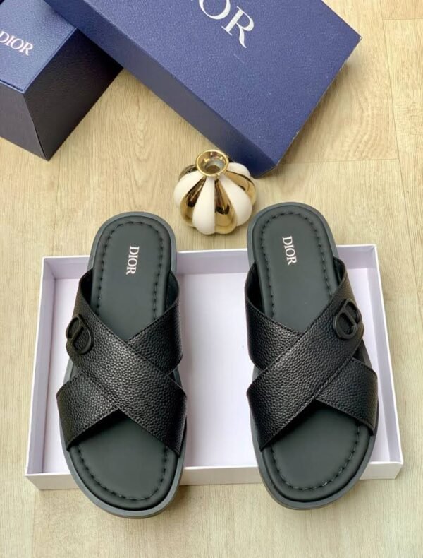 A pair of blue Dior sandals with crisscross straps and gold buckle details, nestled in a white box alongside a navy blue Dior box and a gold decorative item.