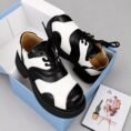 A pair of luxurious black and green shoes with a glossy finish, displayed on a white and blue shoe box with a Vogue magazine.