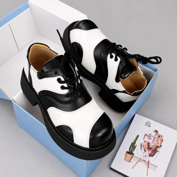 A pair of luxurious black and green shoes with a glossy finish, displayed on a white and blue shoe box with a Vogue magazine.