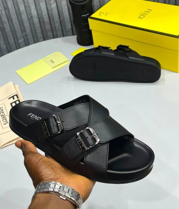 A hand holding a black Fendi slide with silver buckles, showcasing the luxurious design and attention to detail.
