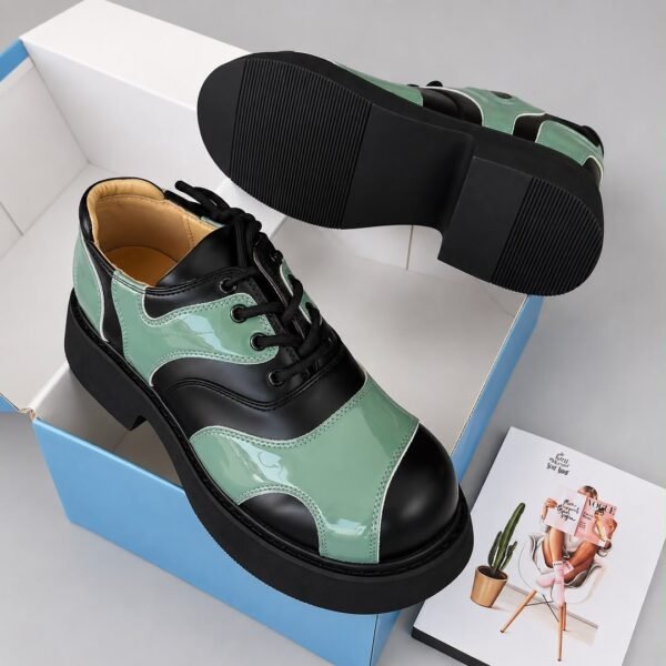 A pair of luxurious black and green shoes with a glossy finish, displayed on a white and blue shoe box with a Vogue magazine.