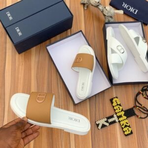 A pair of luxurious Dior slides in white and brown, elegantly displayed in their boxes on a wooden surface.