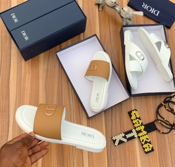 A pair of luxurious Dior slides in white and brown, elegantly displayed in their boxes on a wooden surface.